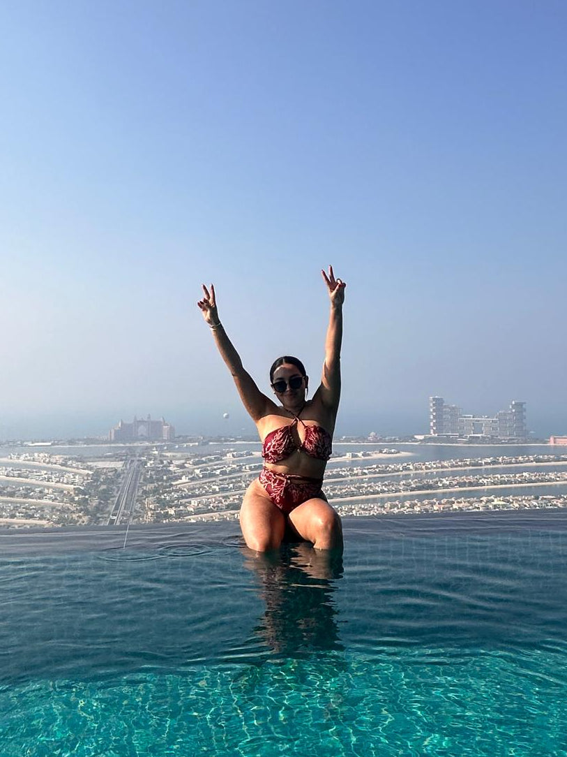 woman in a brazilian luxury swimsuit standing in an infinity pool with a cityscape in the background