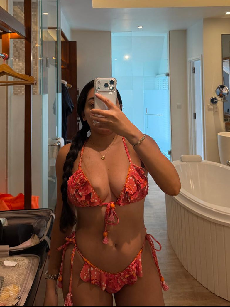 Woman taking a mirror selfie wearing an brazilian orange bikini in a bathroom.